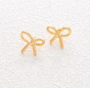 Macro shot of 3D gold bow earrings with polished finish on a white textured background