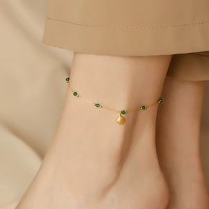 Détail d'une chevillère dorée avec perles vertes et pendentif coquillage au pied