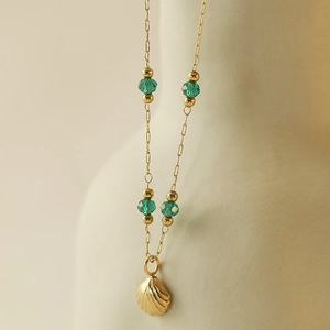 Détail d'un pendentif coquillage doré avec perles vert émeraude sur une chaîne fine