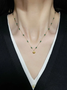 Close-up of a gold scallop shell pendant with emerald green beads on a black knit top