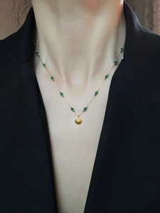 Macro view of shell pendant necklace with emerald green beads on golden titanium chain