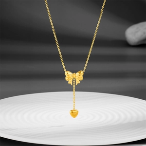 Elegant gold titanium necklace featuring a 3D bow pendant and a heart-shaped tassel drop