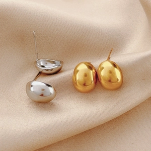 Boucles d'oreilles haricot en acier titane or et argent sur tissu en soie beige