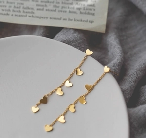Détail de boucles d'oreilles pampilles dorées avec petits cœurs sur chaînes fines