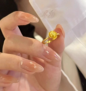 Close-up of a golden rose ring featuring 3D layered petals and a slim metal band