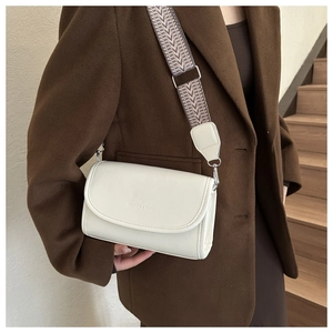 Close-up of white crossbody bag with wide colorful woven strap and silver hardware