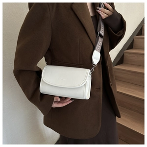 Close-up of white crossbody bag with geometric wide strap on model in brown suit