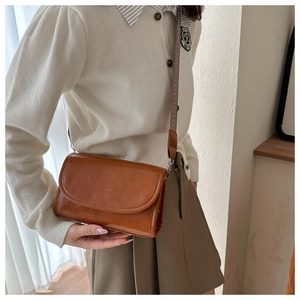Detail of a brown leather crossbody bag with wide patterned strap and embossed text
