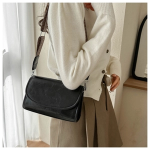 Detail of black leather square bag featuring an embossed logo and a wide patterned strap
