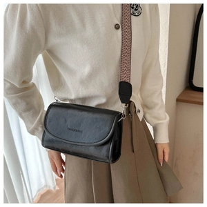 Classic black crossbody bag with wide patterned strap shown in an aesthetic setting