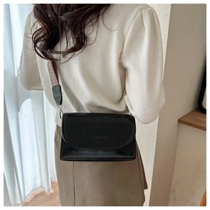 Detailed view of black flap crossbody bag with fashion lettering and wide woven strap