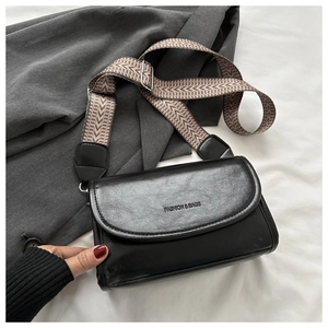 Detail of black crossbody bag with wide geometric pattern strap and silver hardware