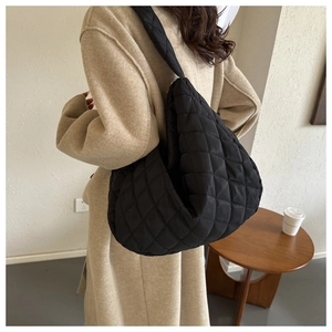 Close-up of a black quilted nylon hobo tote bag worn over the shoulder by a model