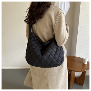 Black quilted puffer shoulder bag with diamond stitching pattern worn with a beige coat