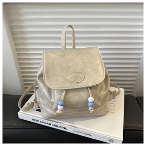 Detail of beige mini backpack with drawstring and blue beaded accents on a display stand