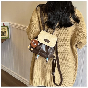 Detail van vintage rugzak met bruine pluche monster hanger op een gebreide trui