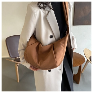 Sac bandoulière demi-lune en nylon marron porté par un mannequin en décor minimal