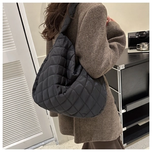 Detail of black quilted nylon tote bag showing the soft padded texture and wide shoulder strap