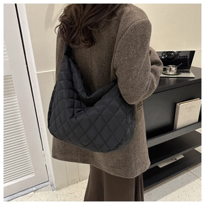 Lifestyle shot of large black quilted nylon tote bag worn by model in a chic indoor setting