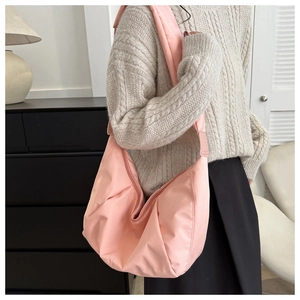 Détail du sac hobo rose plissé en nylon doux avec bandoulière large sur un pull beige