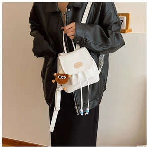 Close-up of white mini PU leather backpack with drawstring closure and plush monster charm