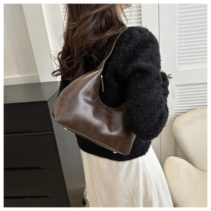 Detail of a brown leather hobo bag worn by a model in a minimalist lifestyle setting