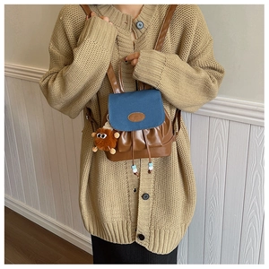 Detail van bruine PU-leren mini-rugzak met blauwe flap en pluchen monster-hanger