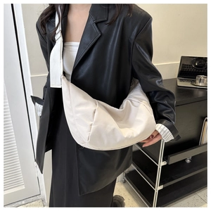 Sac à bandoulière chic en nylon crème porté sur une veste en cuir noir stylée