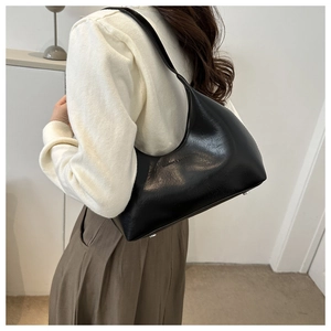 Close-up of black minimalist half-moon shoulder bag showing fine texture and bottom studs