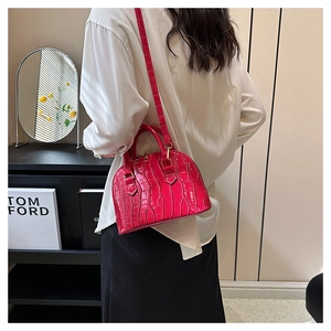 Detail of rose red crocodile pattern shell bag worn over the shoulder in indoor setting