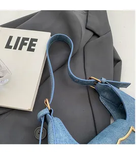 Detail of light blue denim crescent bag with gold buckle on a dark grey blazer