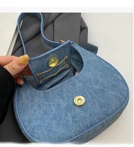 Detail of light blue denim crescent bag showing gold magnetic closure and fabric texture