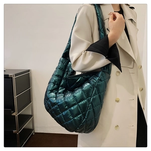 Détail du sac fourre-tout matelassé vert foncé brillant porté par un mannequin en trench