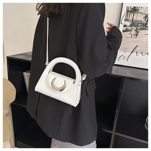 Detailed view of white crossbody bag with silver moon buckle worn by a model