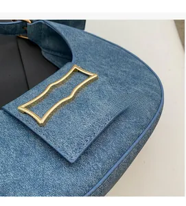 Detailed close-up of dark blue denim shoulder bag with decorative wavy gold buckle
