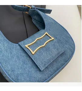 Detail of blue denim shoulder bag featuring a wavy gold buckle and fine stitching