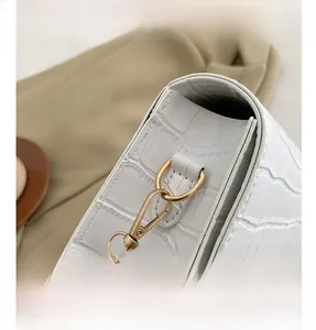 Detail of white crocodile-embossed leather texture and polished gold metal hook clasp
