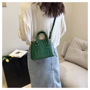 Green crocodile-textured shell bag shown worn as a crossbody purse in a lifestyle setting