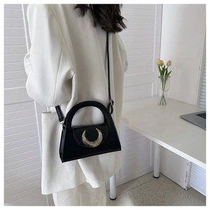 Detail of a black trapezoid crossbody bag with a distinctive crescent metal clasp