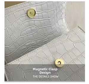Detail of golden magnetic snap closure on white crocodile embossed leather bag