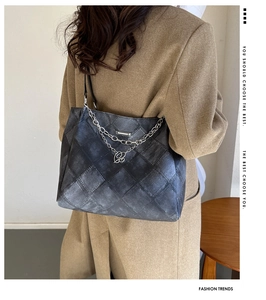 Detail of quilted grey tote bag with silver chain strap worn over a camel coat