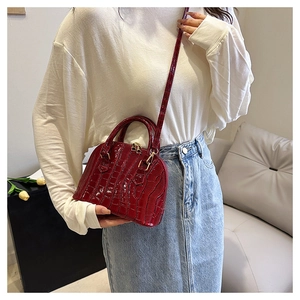 Detail of wine red crocodile effect shell bag with gold hardware on a blue denim skirt