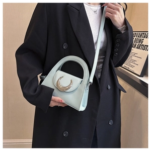 Detail view of mint green handbag featuring a polished metal moon-shaped clasp and handle