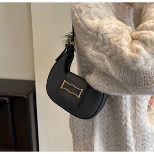 Detail of black leather crescent bag with golden metal buckle and feather decoration
