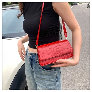 Detail of red crocodile pattern patent leather baguette shoulder bag on a model