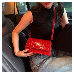 Detailed texture of red crocodile-patterned patent leather shoulder bag with gold buckle