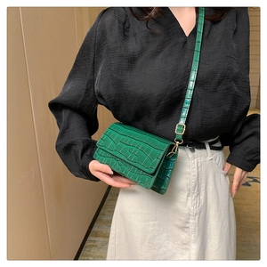 Detail of bright green crossbody bag featuring textured crocodile pattern and slim strap