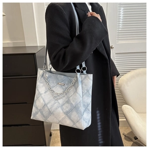 Close-up of denim tote bag with quilted pattern and decorative metal chain charms