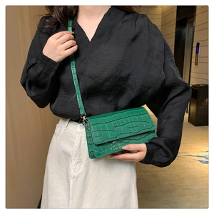 Detail of bright green faux crocodile pattern flap shoulder bag worn by a fashion model