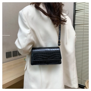 Detail of black crocodile texture shoulder bag with gold buckle on white blazer